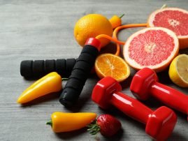 Healthy food, skipping rope and dumbbells on gray textured background