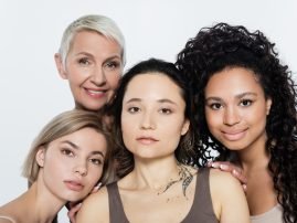 Smiling interracial women hugging tattooed friend isolated on grey, feminism concept